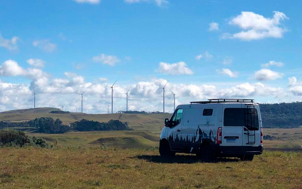 Motorhome estacionado em terreno panorâmico em frente a um parque eólico, fazendo uma viagem tranquila por utilizar dicas e truques.