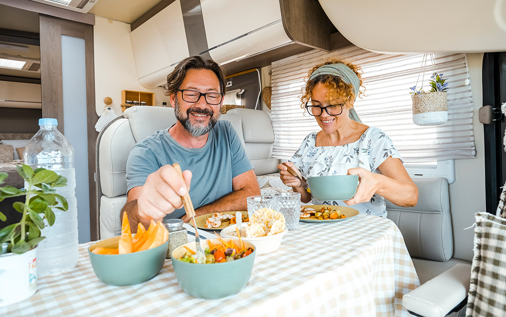 Imagem de um casal fazendo suas refeições em uma viagem de motorhome.