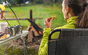Imagem de uma mulher que foi acampar de motorhome e está aproveitando a paisagem tomando um café da tarde.