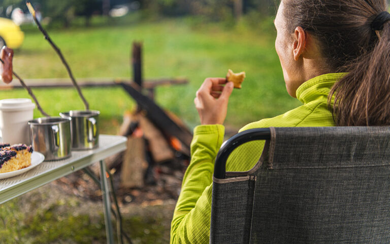Imagem de uma mulher que foi acampar de motorhome e está aproveitando a paisagem tomando um café da tarde.
